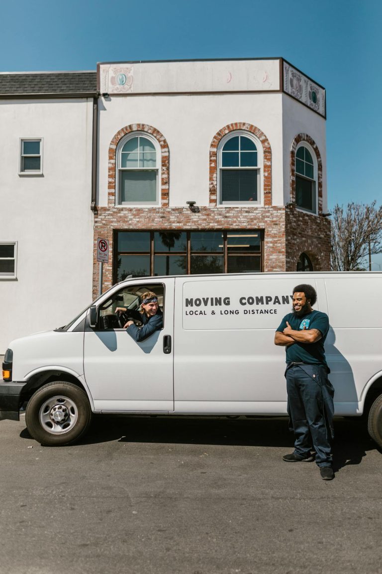 Man in Blue Long Sleeve Shirt and Blue Denim Jeans Standing Beside White Van